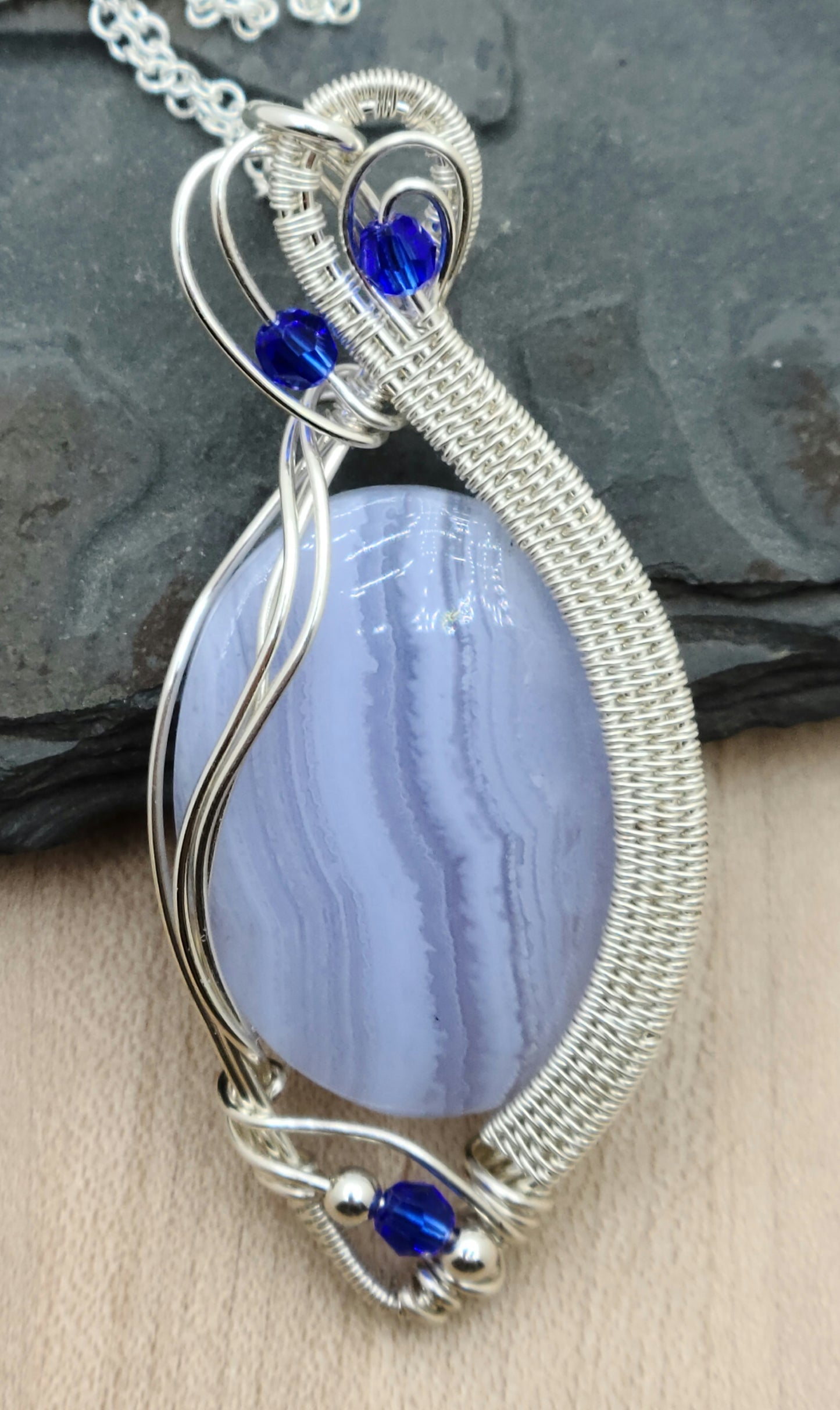 Enjoy the calming effect of this lovely blue lace agate stone pendant, with its frame woven from tarnish resistant silver plated copper & adorned with bright blue crystals.