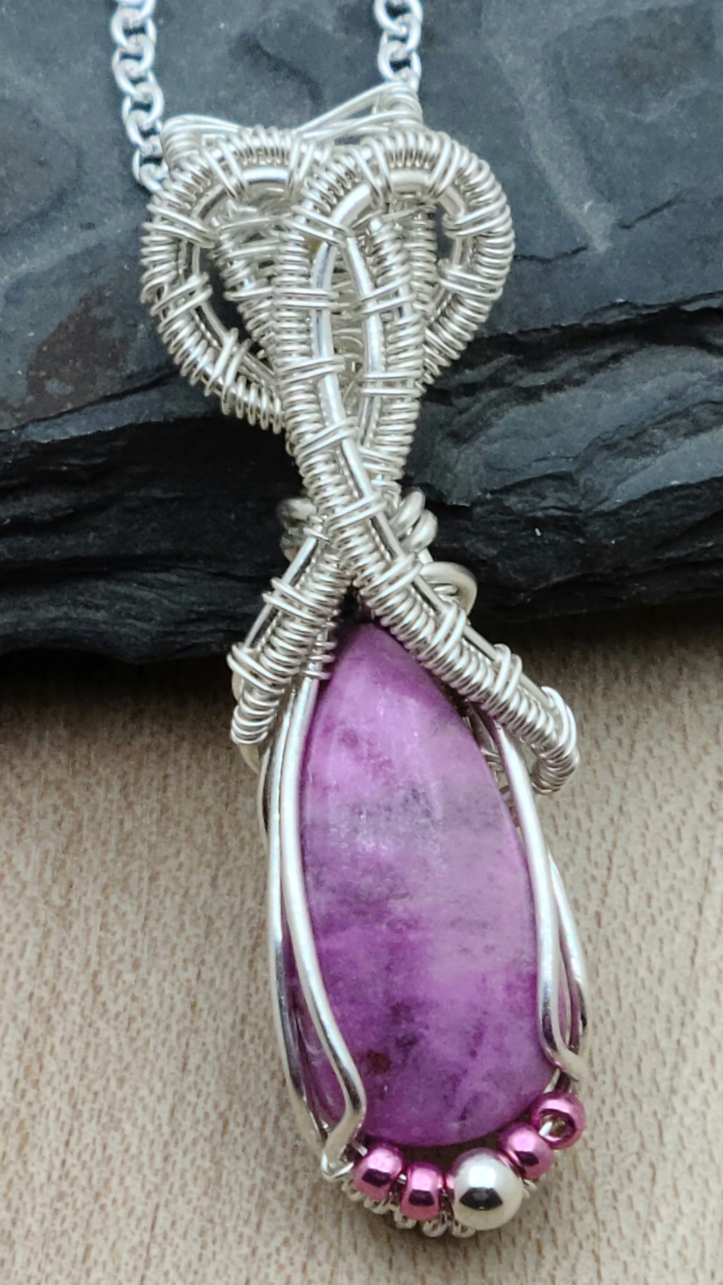 This delicate pinkish stone (with a subtle purple hue) is associated with emotional healing, love, & joy. The intricate 'frame' is woven from silver filled wire.