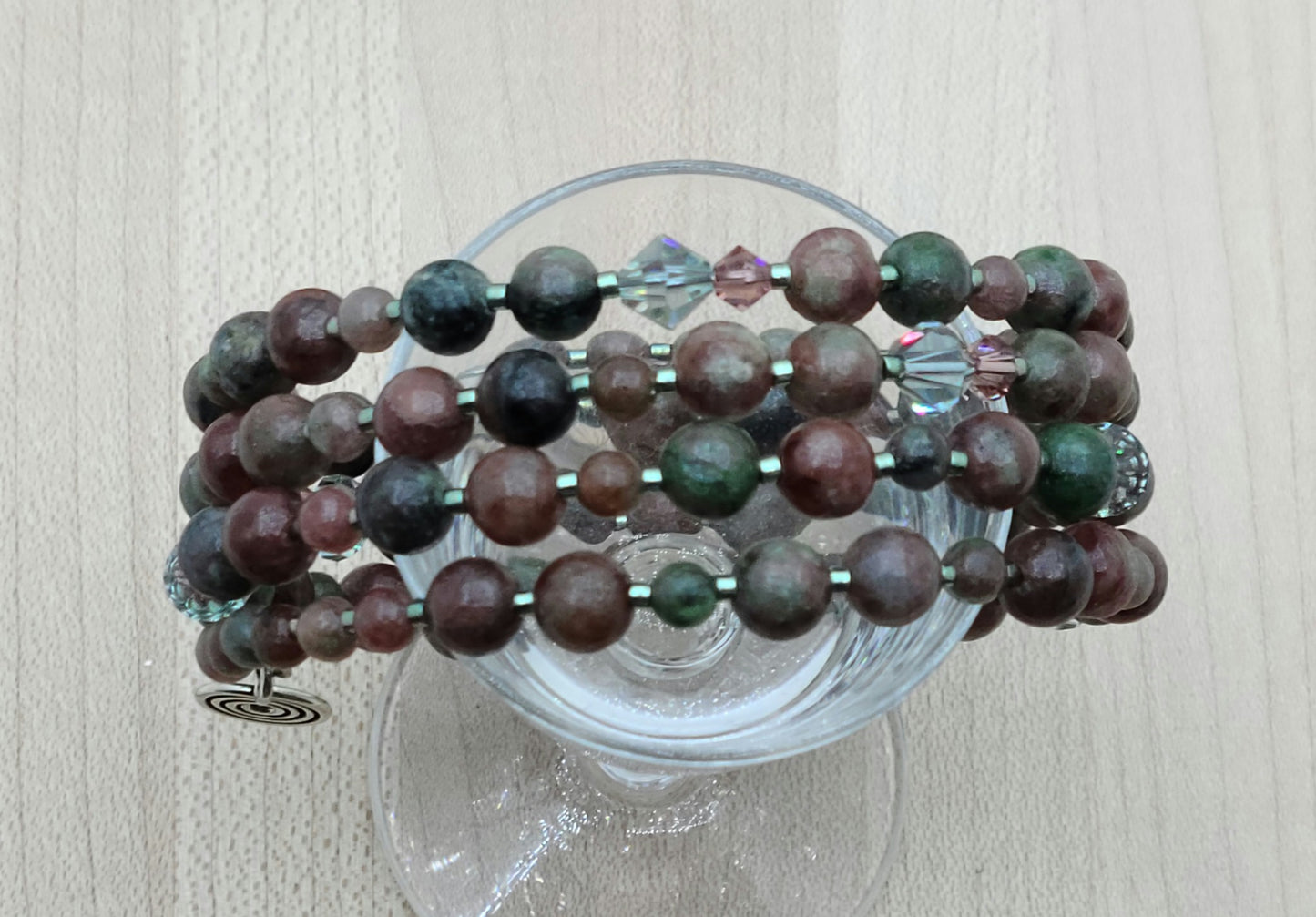 The mixed, earthy color palette of burgundy, forest green, black, & white swirls in Kashgar garnet are paired with pale green & vintage rose crystals & green Miyuki delica to create a lovely 4 row memory wire bracelet.