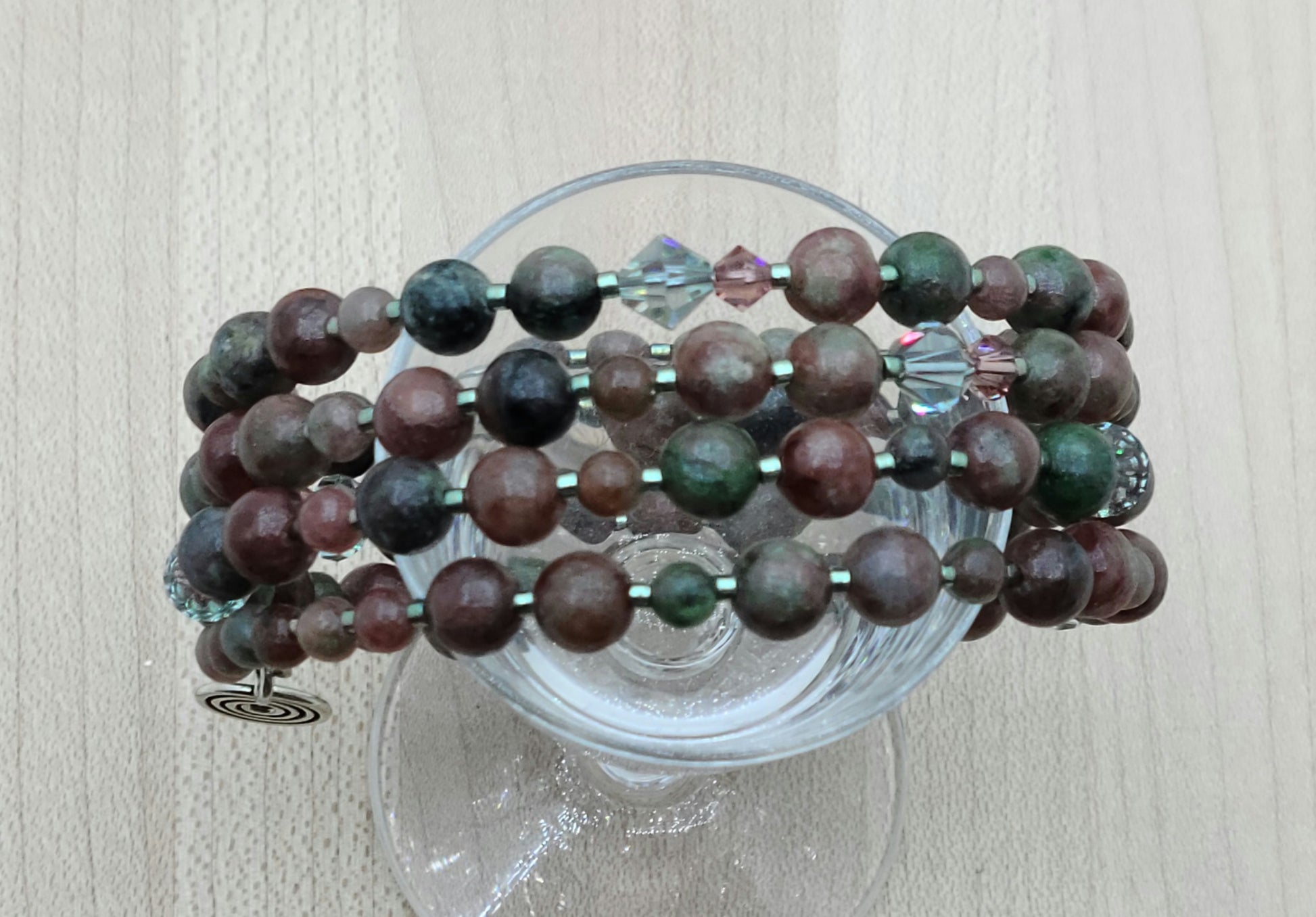 The mixed, earthy color palette of burgundy, forest green, black, & white swirls in Kashgar garnet are paired with pale green & vintage rose crystals & green Miyuki delica to create a lovely 4 row memory wire bracelet.