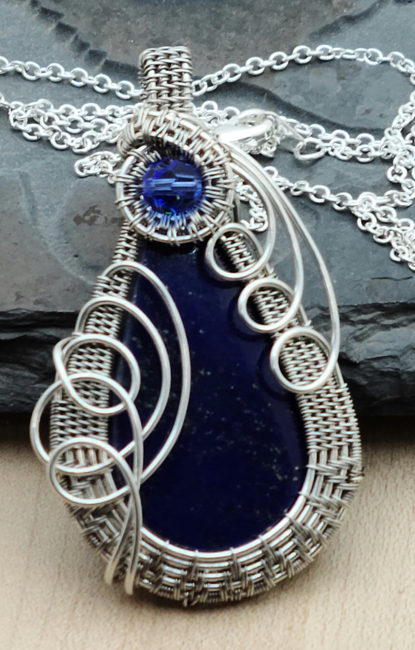 Deep blue lapis lazuli cabochon framed by silver filled woven wire & accented with a sapphire blue crystal.