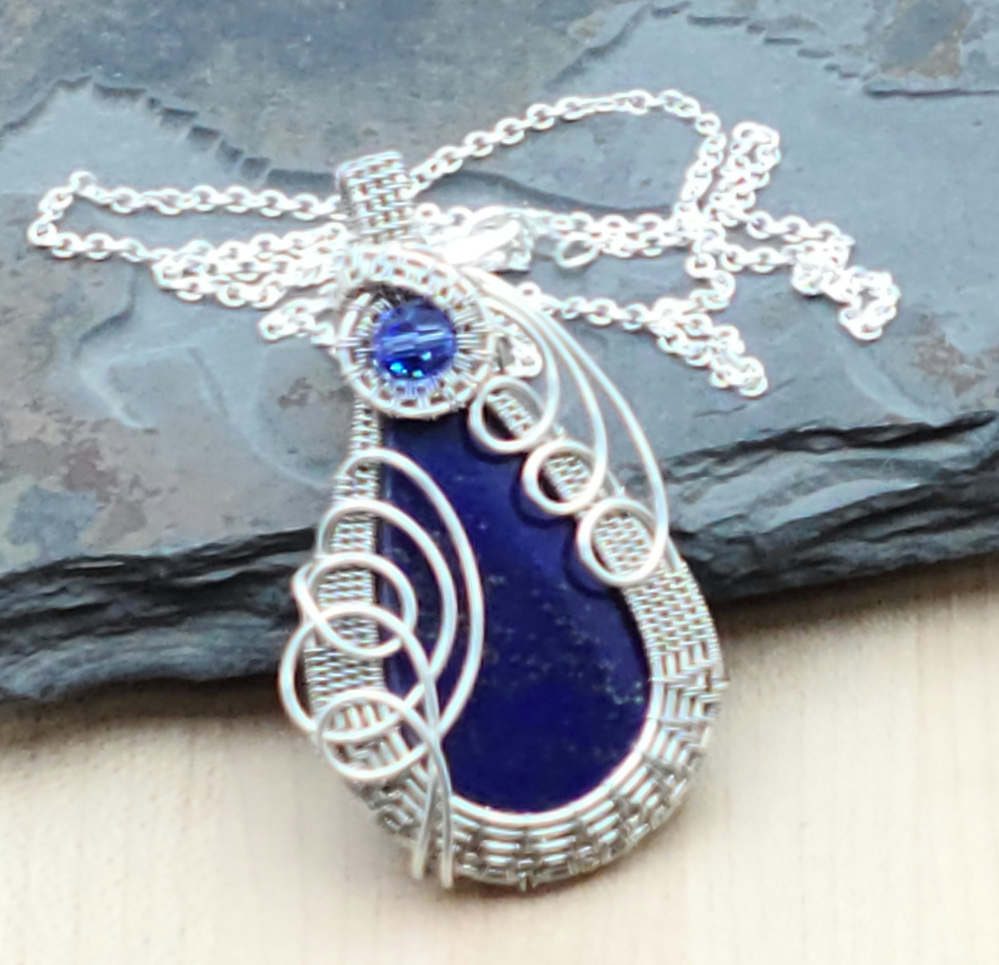 Deep blue lapis lazuli cabochon framed by silver filled woven wire & accented with a sapphire blue crystal.