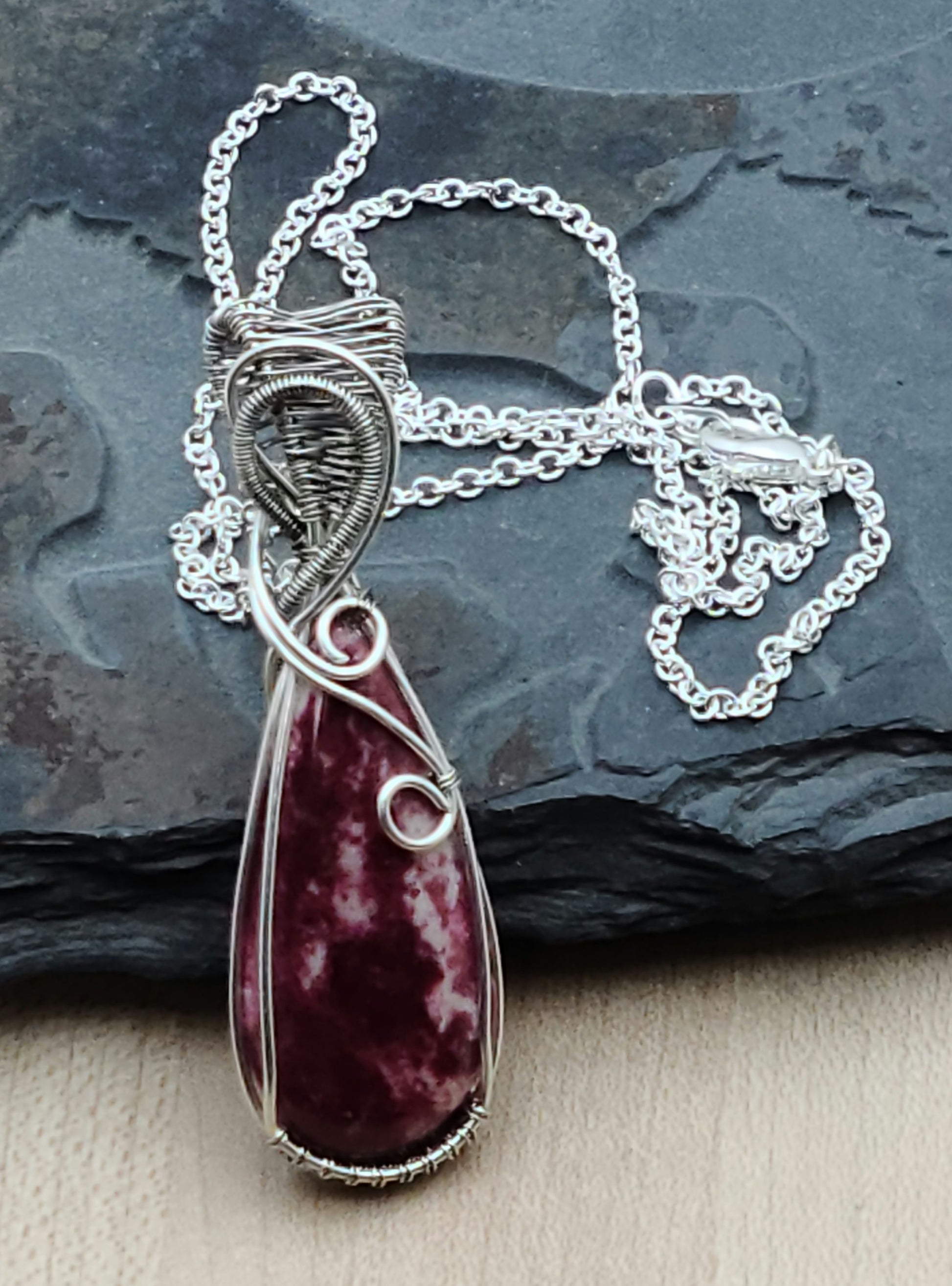 Pink thulite is a stone of the heart chakra, said to open pathways to unconditional love, compassion, and kindness. This pendant features expertly woven silver filled and antiqued silver filled wire—much more silver than plating—carefully sculpted into an design that showcases the stone's gentle light-to-dark pink gradations.