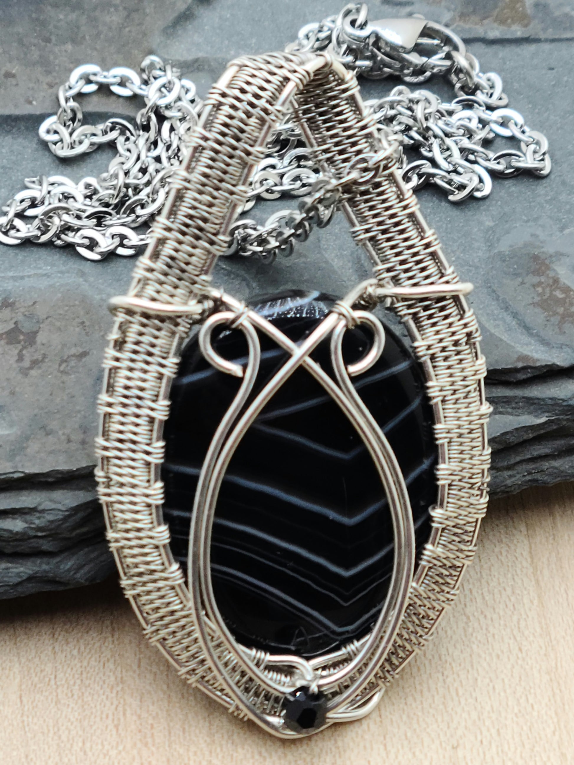 Beautiful white banded black onyx cabochon expertly framed with an intricately woven pattern of silver filled &amp; antique silver filled wire. This stone is traditionally associated with self-control, clear decision making, and self-confidence.
