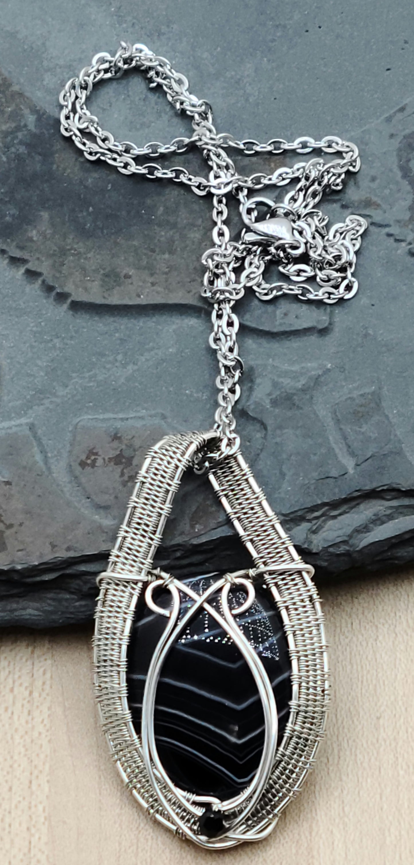 Beautiful white banded black onyx cabochon expertly framed with an intricately woven pattern of silver filled &amp; antique silver filled wire. This stone is traditionally associated with self-control, clear decision making, and self-confidence.