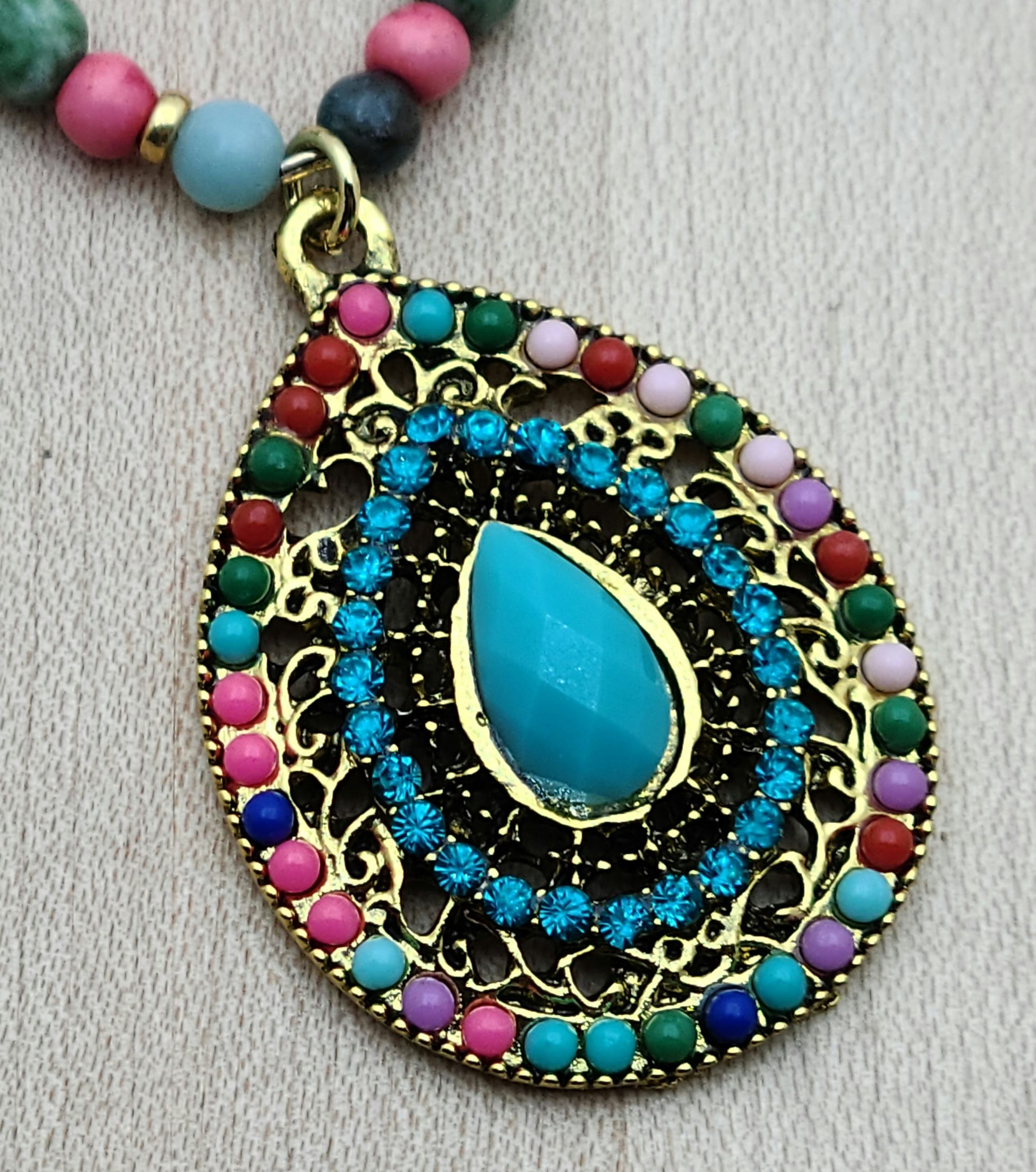 Fun and vibrant, this pendant necklace captures attention with its bold design and bright, happy colors of turquoise, bright pink, green, & gold.