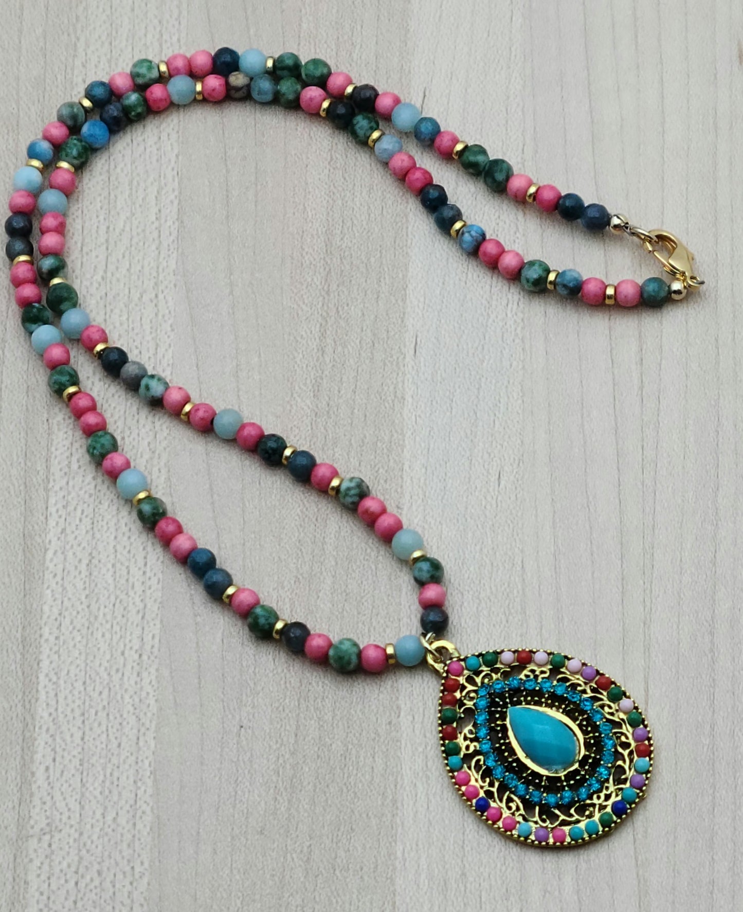 Fun and vibrant, this pendant necklace captures attention with its bold design and bright, happy colors of turquoise, bright pink, green, & gold. the findings are gold fill.