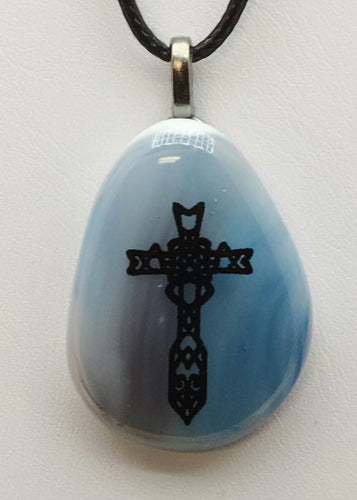 This exquisite pendant features an elaborate cross design, elegantly displayed against a background of blue and mauve fused glass.