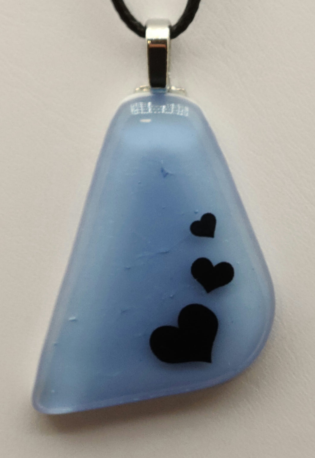 This shimmering fused glass pendant features an iridescent blue background with three floating hearts.