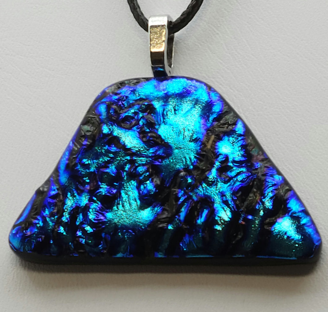 This deep peacock purplish blue fused glass pendant features a unique uneven triangle shape and a mesmerizing ripple dichroic effect.