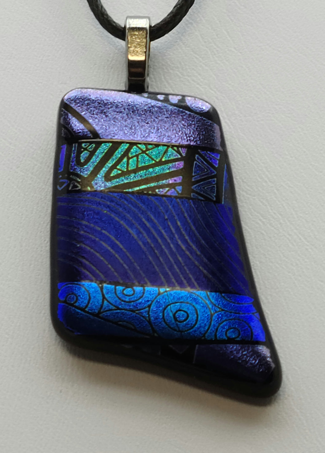 This dainty fused glass pendant showcases beautiful hues of blue and purple, etched in dichroic glass and fired to a satin smooth finish.