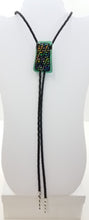 bolo tie of Geometric gold with black, green, & purple dichroic glass backed by translucent green glass with black leather